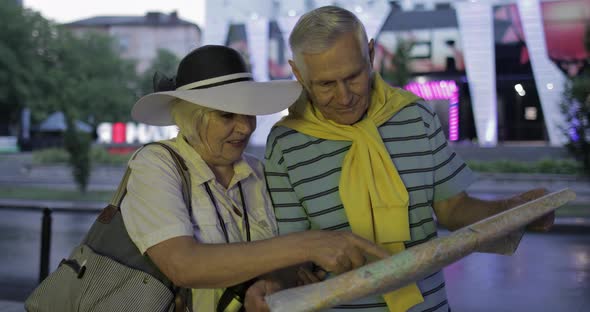 Senior Male and Female Tourists Standing with a Map in Hands Looking for Route