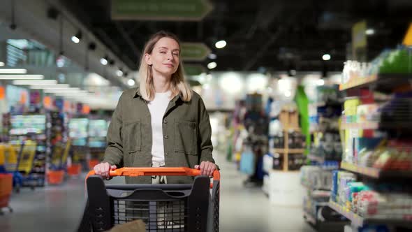 young happy woman pushing trolley spends time in a supermarket or mall store.