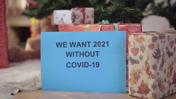 Closeup of Paper with We Want 2021 Without Covid19 Written and Blurred Packed Christmas Gifts at
