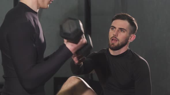 Handsome Bearded Male Personal Trainer Helping Young Man at the Gym