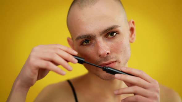 Closeup Portrait of Confident Queer Man Posing with Mascara at Yellow Background