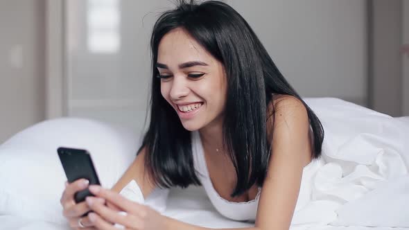 Pretty Girl in Bed Reads Messages on Smartphone and Smiles