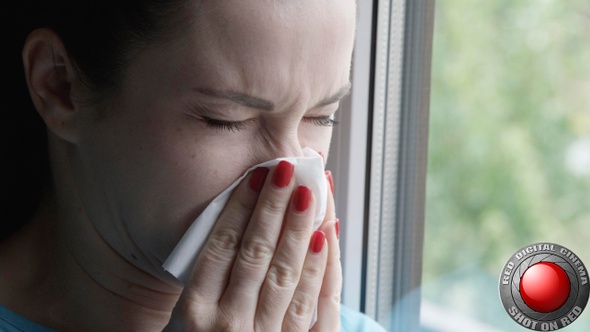 Woman Sneezing Into A Napkin Standing By The Window