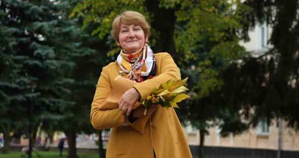 Beautiful Mature Woman Holding a Bag in Her Hands and Smiling at the Camera in the Autumn Park