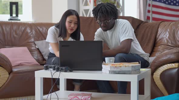 Wide Shot Portrait of African American Man and Asian Woman Surfing Internet on Laptop Talking in