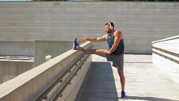 Young Man in Headphones Stretching Leg Outdoors