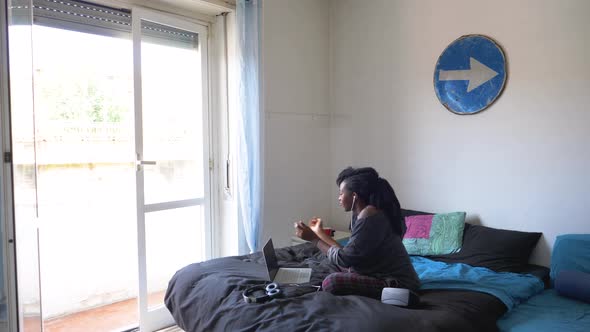 Young woman sitting on bed dancing while listening music at laptop