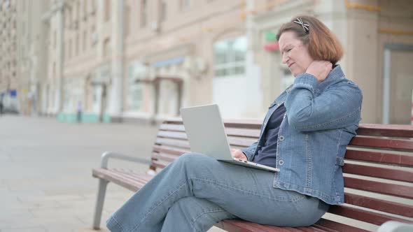 Old Woman with Neck Pain Using Laptop While Sitting Outdoor on Bench
