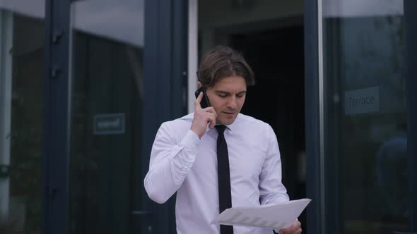 Confident Man Walking with Paperwork on Office Terrace Talking on Phone Smiling