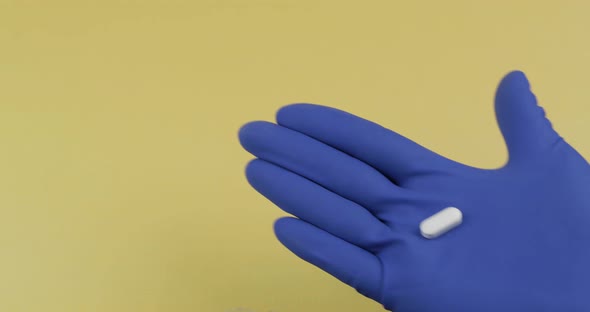 One Oval White Pill in Hand Dressed in Rubber Sterile Medical Glove