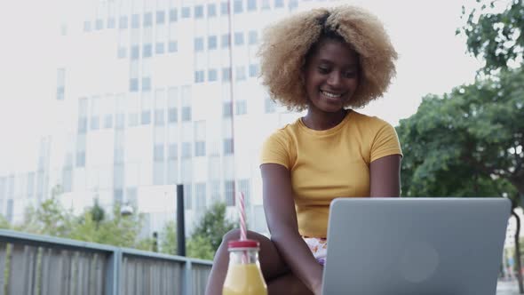 Young Black American Woman Using Laptop Computer While Sitting on Bench Outdoors