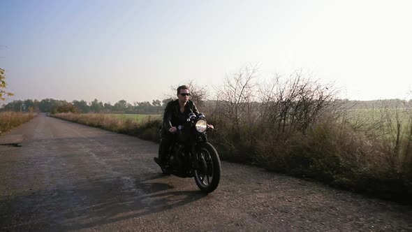 Stylish Cool Young Man in Sunglasses and Leather Jacket Riding Motorcycle on a Asphalt Road on a