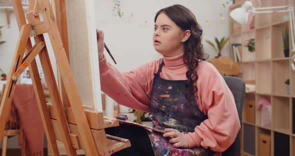 Young Talanted Teenager Wearing Artists Apron Painting While Sitting in Front of Molbert at Her Room