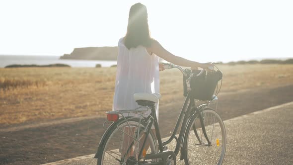 Panning Shot of Confident Woman Walking in Sunbeam with Bike at Background of Mediterranean Sea and