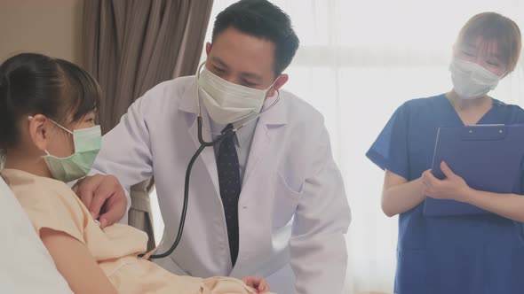 Asian doctor measure heart rate by stethoscope on little kid patient on bed in recovery room.