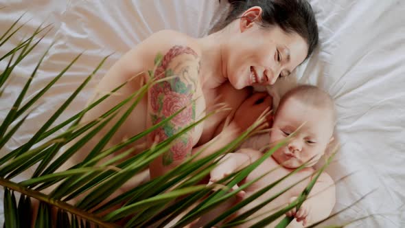 Loving Asian Young Mommy Hugging Soothing Adorable Sweet Baby Boy Lying in Bed