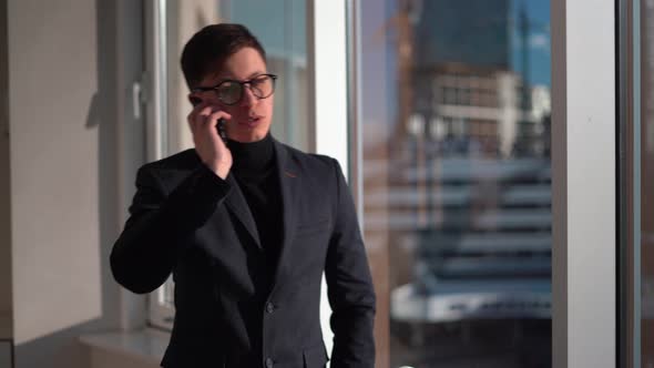 Caucasian Businessman in Glasses Talking on the Phone While Standing at the Window Business