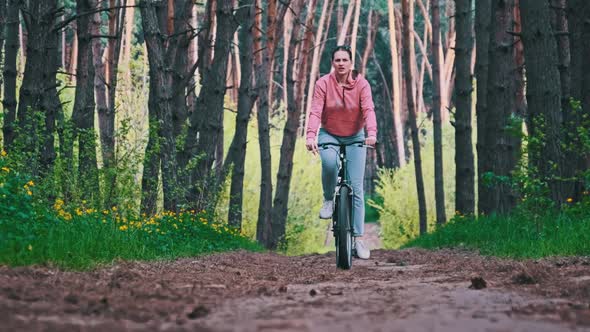 Woman on Bicycle Rides on Forest Path Between Green Trees Slow Motion