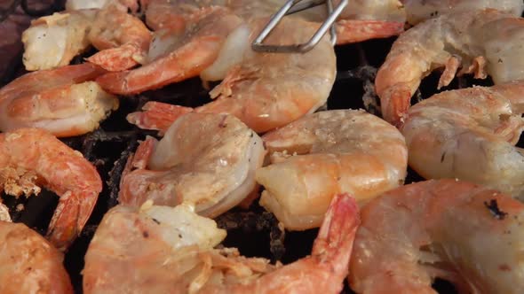Closeup of Large Grilled Shrimps Rotating with Kitchen Tongs on the Grill Grid