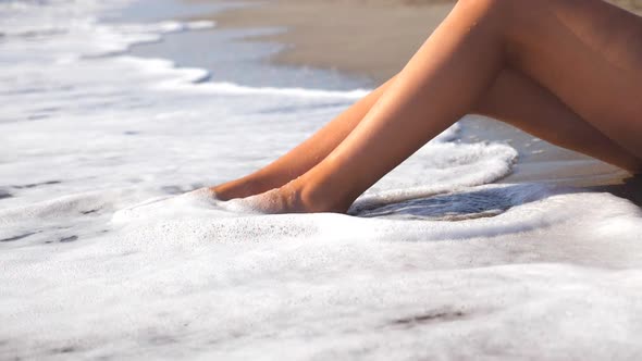 Sea Waves Washing Over Tanned Female Feet. Beautiful Young Woman Relaxing on Coast During Summer