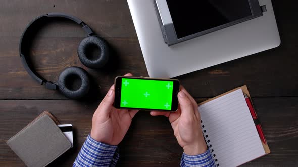 Hands of Man Using Smartphone with Green Screen on Wood Table