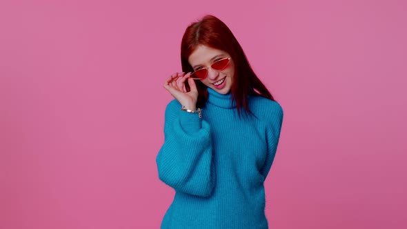 Sincere Cool Cheerful Redhead Girl in Blue Sweater Wearing Sunglasses Charming Smile on Pink Wall