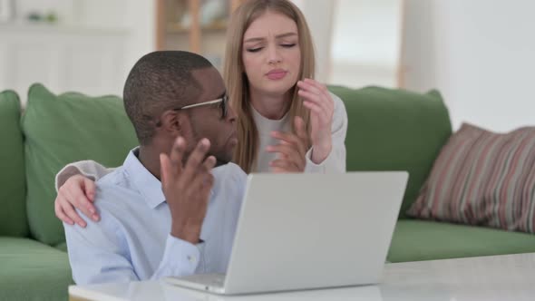 Mixed Race Couple Reacting To Loss While Using Laptop at Home