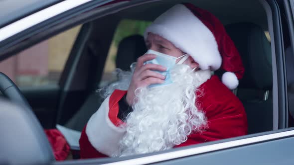 Ill Santa Clause in Coronavirus Face Mask Coughing Sitting in Car Outdoors