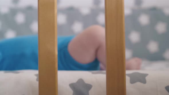 Little Child with Bare Legs Licks Hand Resting in Modern Cot