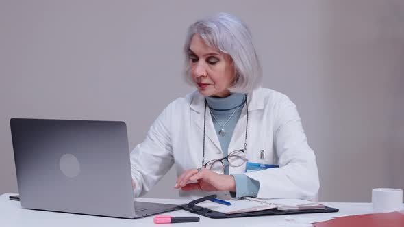 Female Doctor Talking with Patient in Video Chat on Laptop in White Office