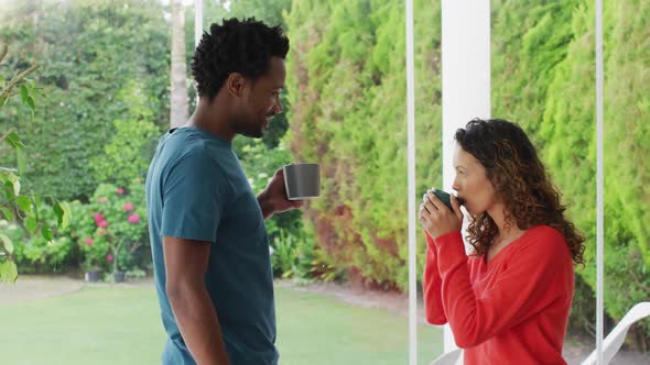 Happy biracial couple relaxing and drinking coffee together on patio