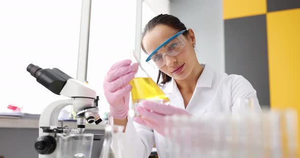 Woman Chemist Looks at the Yellow Liquid in the Flask