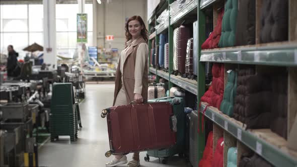 Young Attractive Female Shopper Choose a Wheeled Travel Suitcase in a Travel Store for Vacation