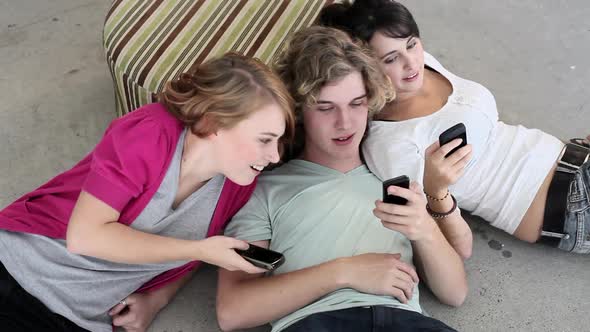 Three teenagers lying on floor looking at smartphones