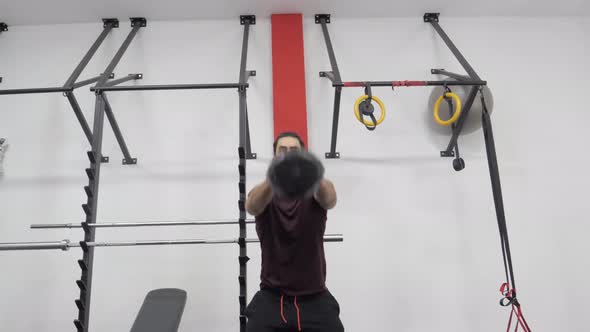 Man lifting kettlebell weight for karate indoors with both hands in the gym