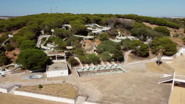 Aerial trucking shot of abandoned historic waterpark during sunny day in Portugal,between green tree