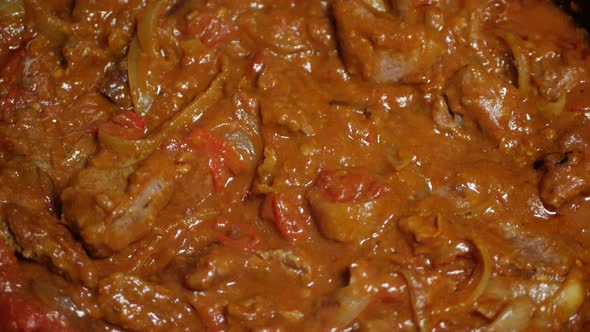 Indian beef curry being slow cooked. Lid  is red to reveal the food. CLOSE UP.