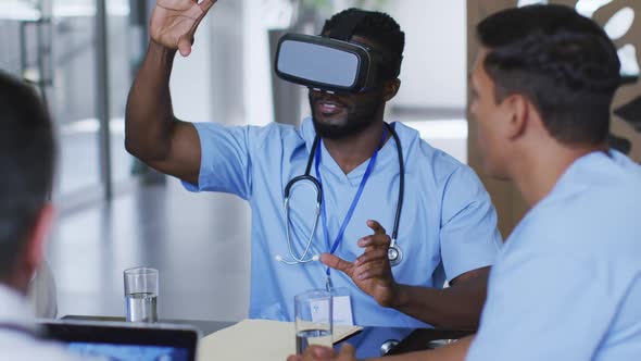 African american male doctor at table using vr headset with a diverse group of colleagues watching