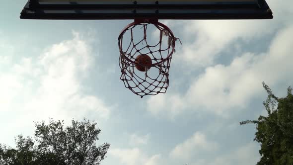 Thrown Orange Basketball Hits the Basket on an Outdoor Court in the Shade of Trees