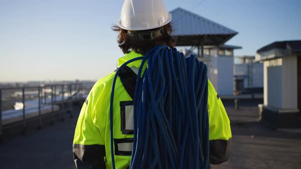 Industrial Climber with Rope Skein Walks to Rooftop Edge