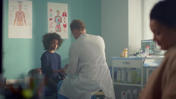 Doctor Putting Pulse Oximeter on Girl Patient Finger Sitting Clinic with Mother