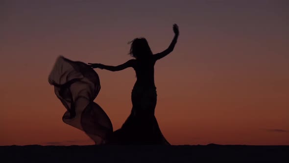 Dancer Holds a Veil in Her Hands, She Dances a Belly Dance on the Beach. Silhouette