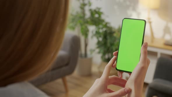 Back View of Woman at Living Room Using Phone With Green Mockup Screen Chroma Key Without Track