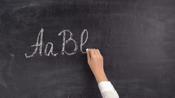 The teacher writes letters of the English alphabet on a chalkboard. The concept of learning English
