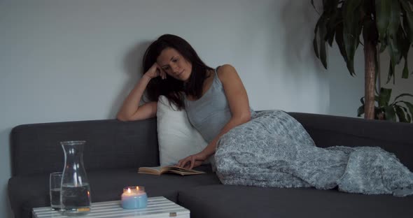 Young Woman at Home Sitting on Sofa Relaxing in Her Living Room Reading Book