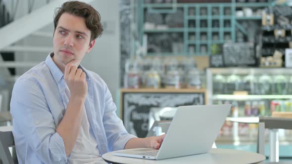 Young Man with Laptop Thinking in Cafe