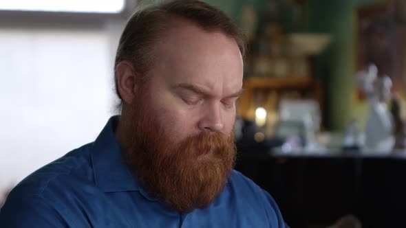 Man with big red beard leaning his head on his hands