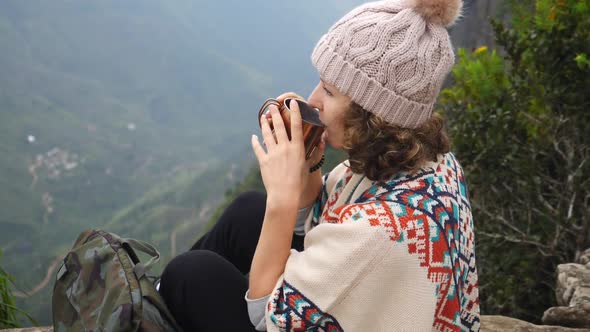 Young Woman Traveler Drinking Hot Tea After Hiking On Cliff Peak