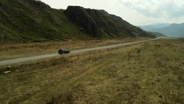 The SUV is Moving Along an Unpaved Road Against the Backdrop of Mountain Peisaage