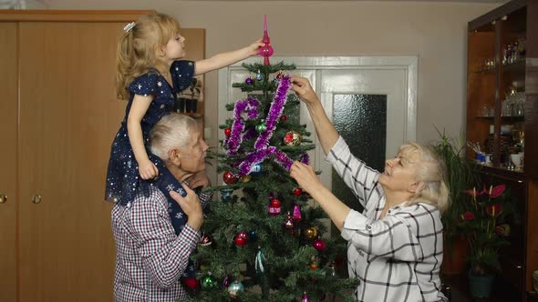 Little Cute Child Girl with Senior Grandparents Family Decorating Artificial Christmas Tree at Home